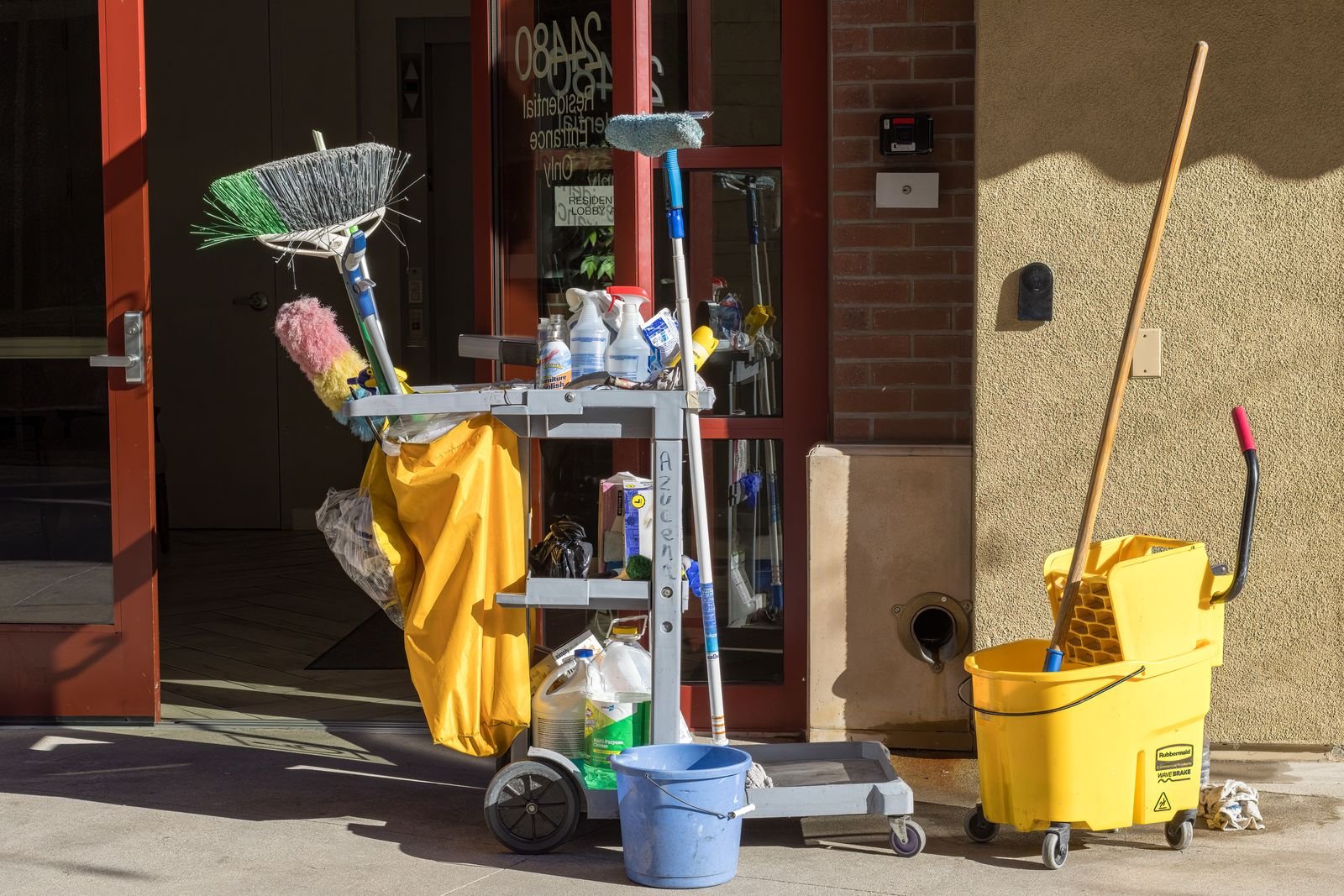 Caretaker cleaning trolley and equipment at a Manchester building entrance