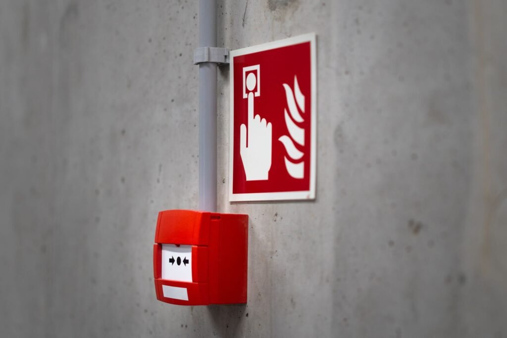 A red fire alarm call point beside a fire safety sign