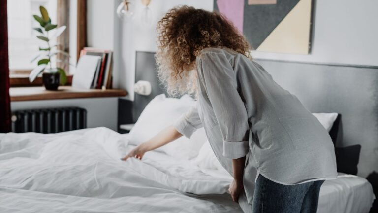 Cleaner making up a bed with fresh white linen in a bright bedroom